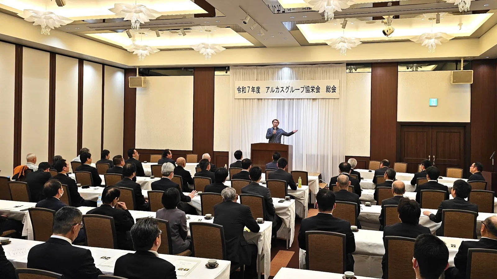 経営者の集まる総会でAI活用について話すマジシャン・コンプレッサー